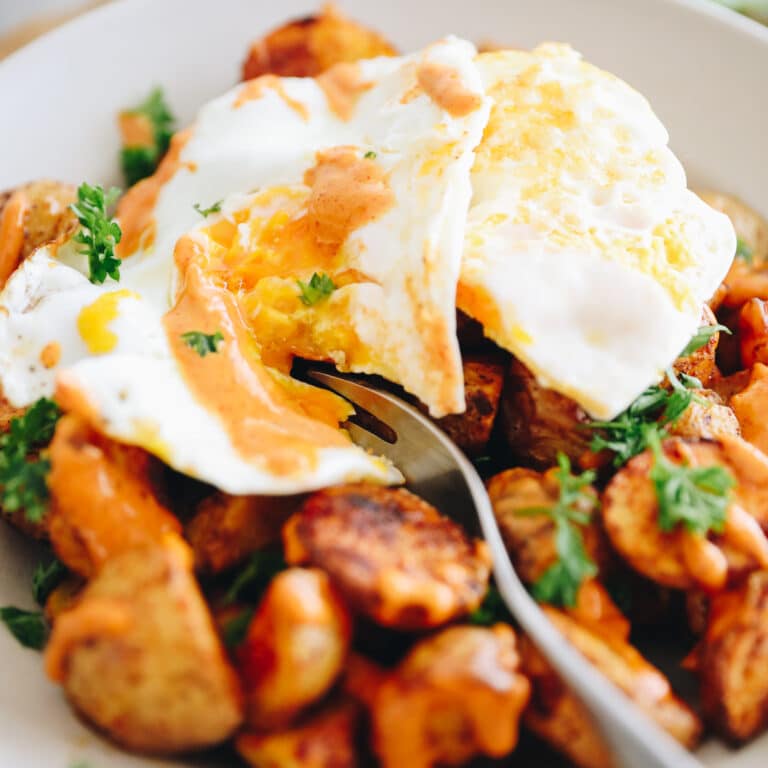 Patatas bravas with a fried egg on top. Silverware cut into egg.