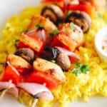 Chicken kabobs served over a bed of rice on a white plate.