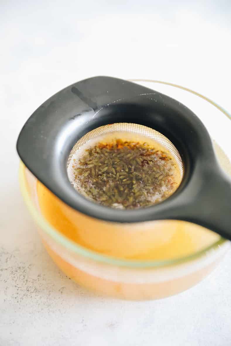 straining lavender buds through a fine mesh strainer in a lavender simple syrup.