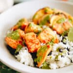 Piri piri chicken in a white bowl served with white rice, black beans and a green sauce.