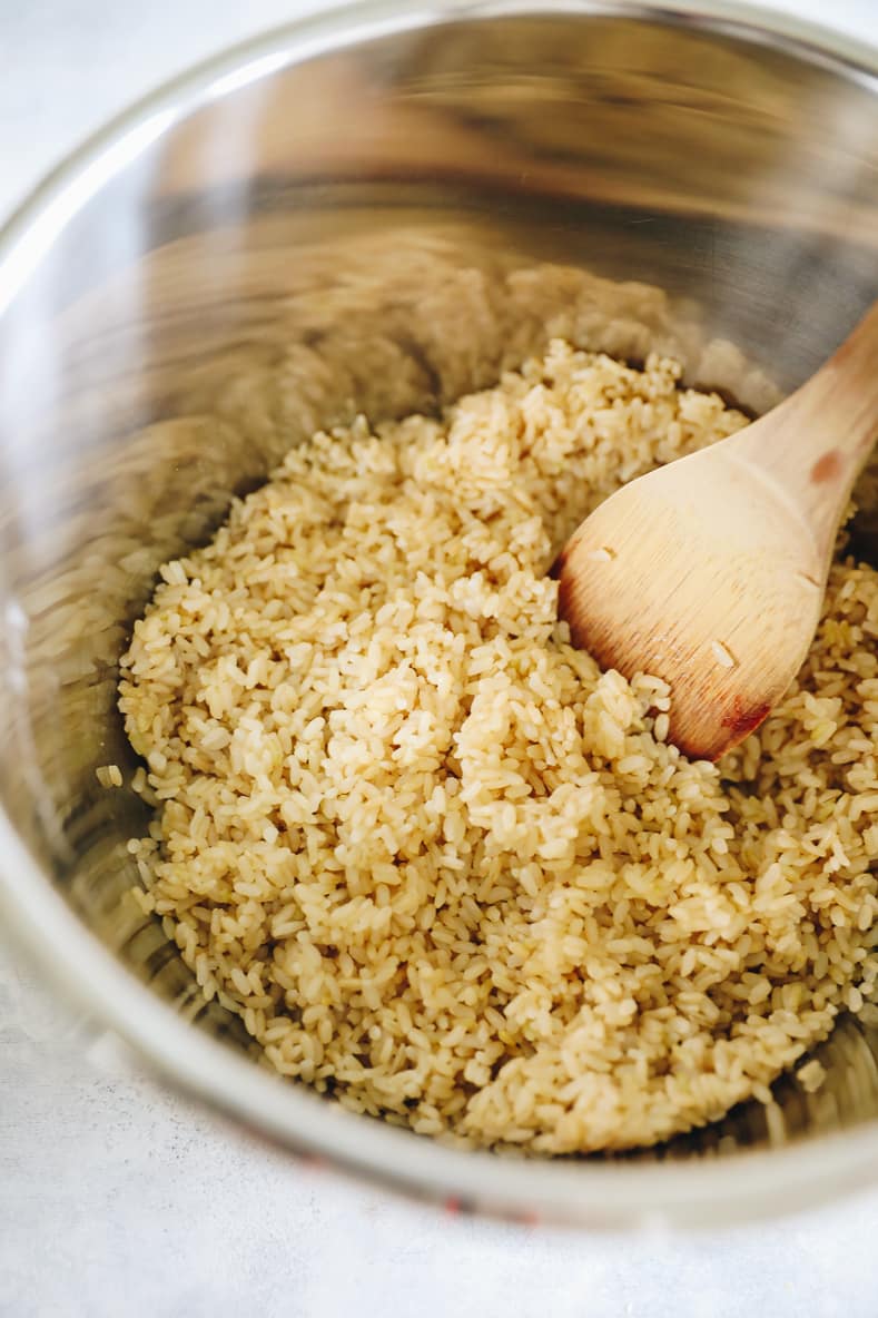 Brown rice in large pot. Wooden spoon stirring rice.