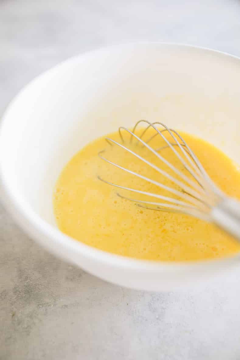 White mixing bowl with eggs and a whisk.