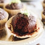 One chocolate zucchini muffin in focus with a bite taken out of it.