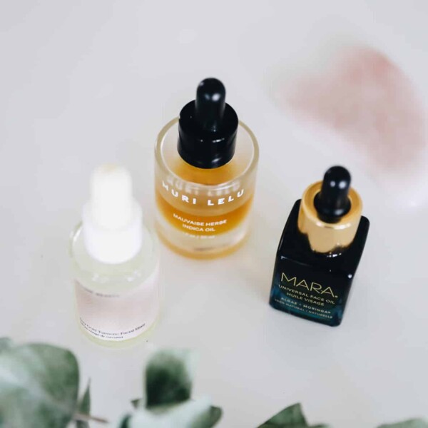 Three jars of facial oils with a sprig of eucalyptus in the foreground.