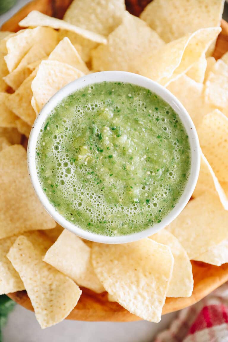 Overhead shot of platter of tortilla chips and a small dish of green salsa in the center.