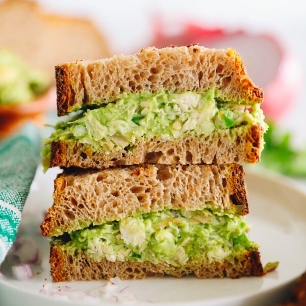 Close up shot of guacamole chicken salad sandwich on thick slices of wheat bread. Two halves of the sandwich are stacked on top of each other with the middle facing the camera.