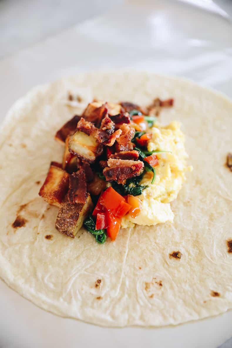 Layered ingredients in a tortilla to be wrapped for breakfast burritos.