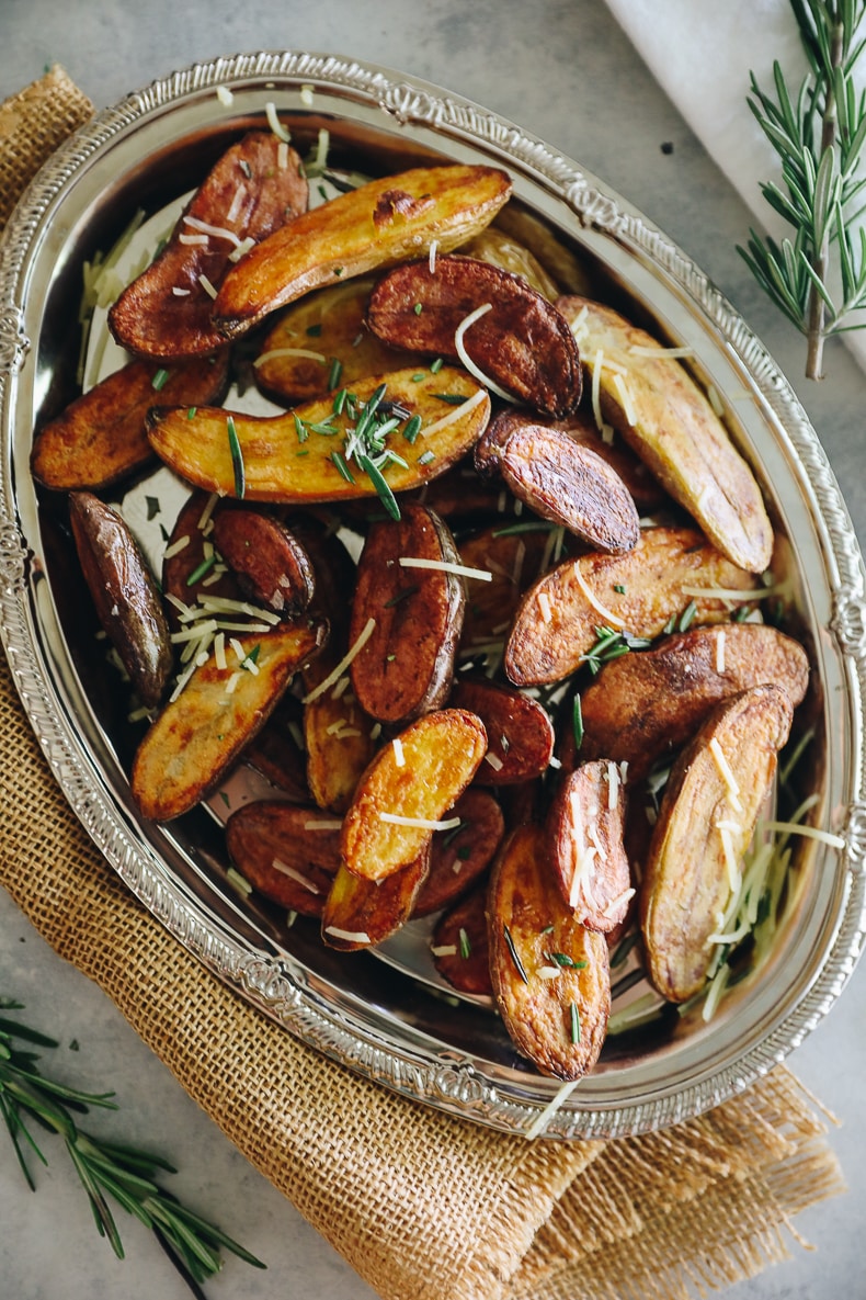 Roasted fingerling potatoes on a silver platter topped with rosemary and parmesan cheese.