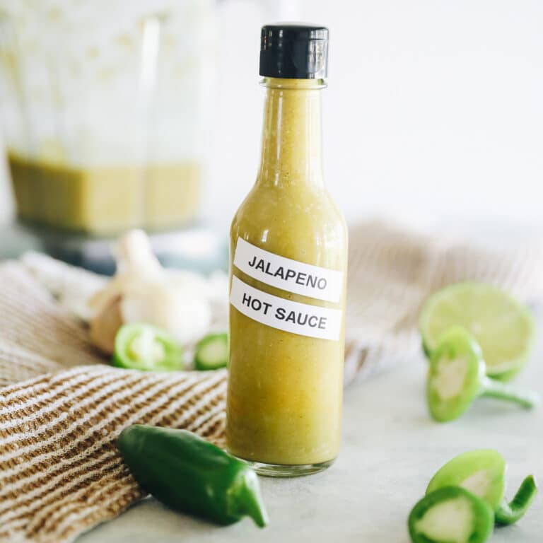 Green Jalapeno Hot Sauce in a tall thin bottle scattered with jalapenos around