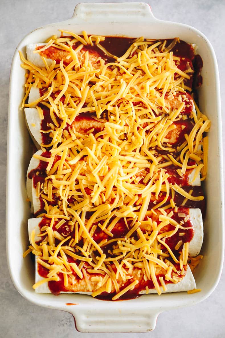 black bean enchiladas covered in enchilada sauce and shredded cheese before going in the oven.