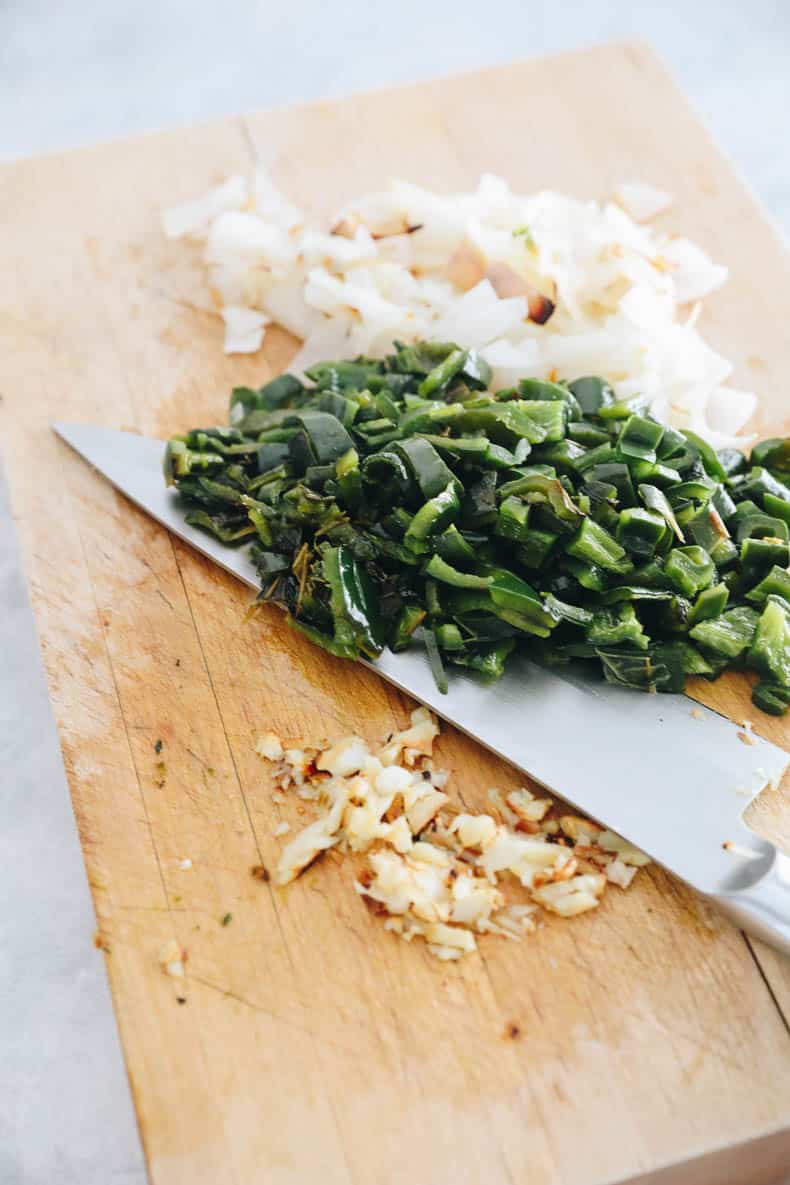 cutting board with chopped poblano peppers, jalapeno peppers, garlic and onion.