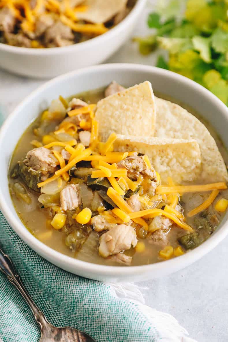 spicy green chili in a bowl topped with shredded cheddar, lime and tortilla chips.