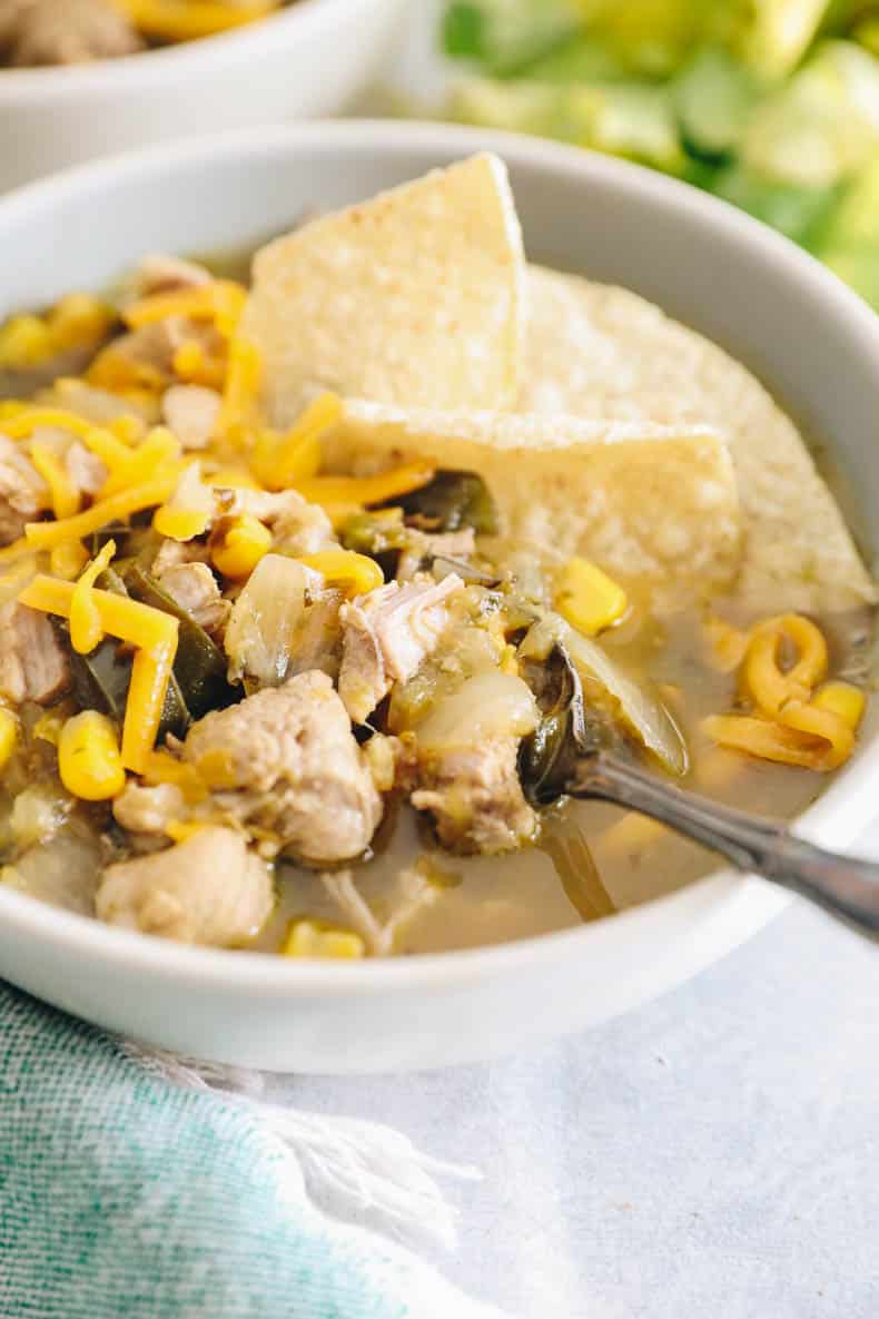 bowl of green chicken chili with shredded and cheese and tortilla