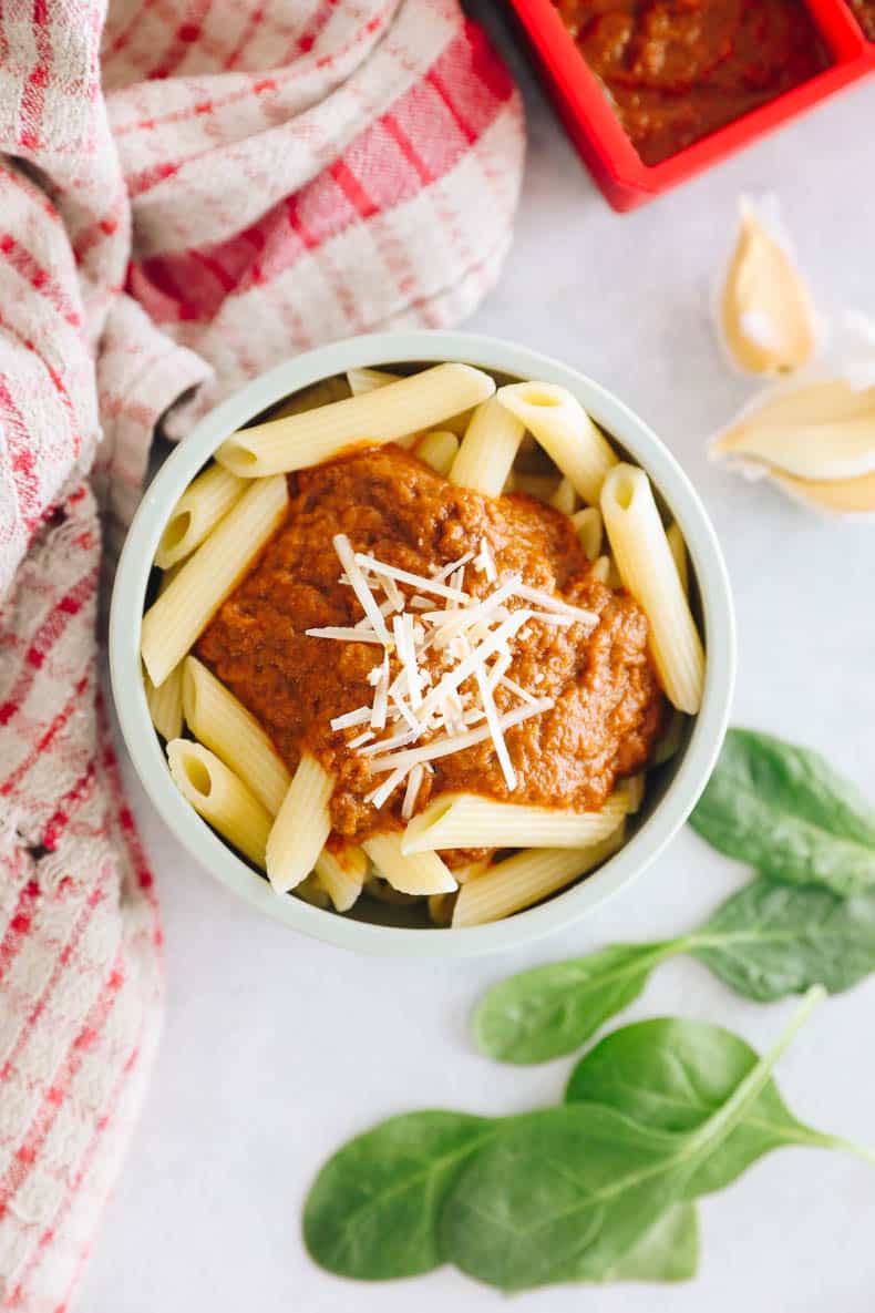 overhead photograph of penne in a baby bowl with tomato sauce and sprinkled parmesan cheese