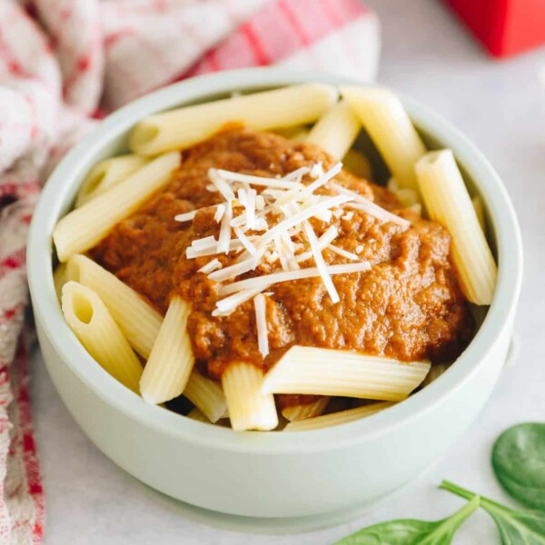 hidden veggie pasta sauce on penne pasta in a green kids bowl topped with parmesan cheese.