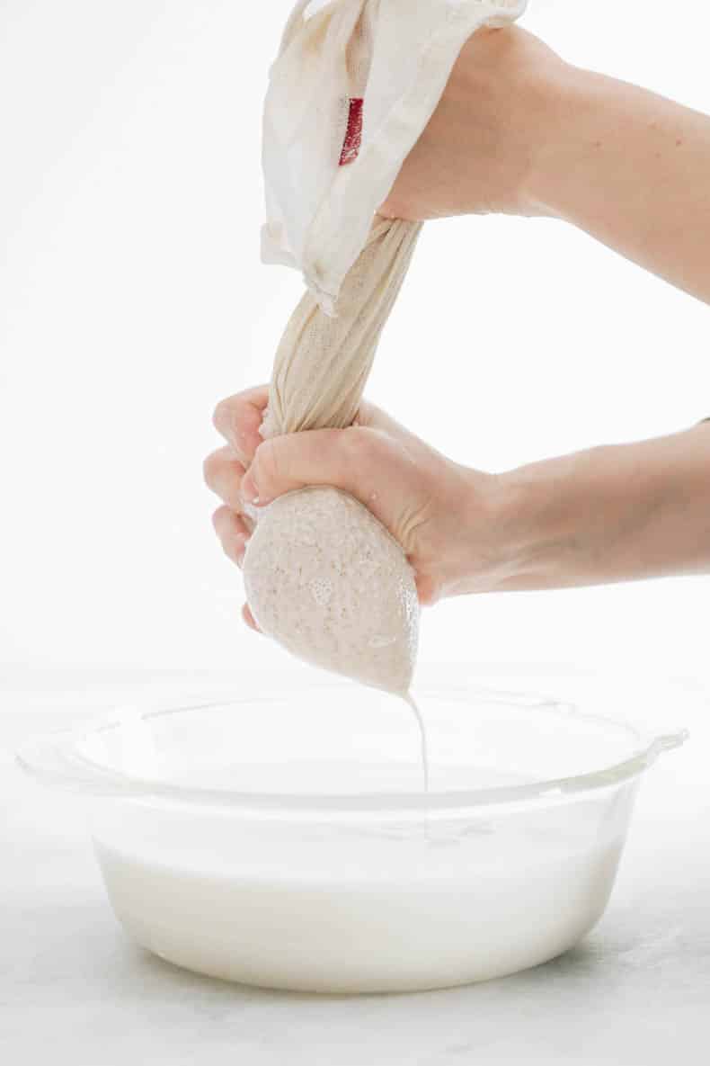 squeezing almond milk out of a nut milk bag into a glass bowl.