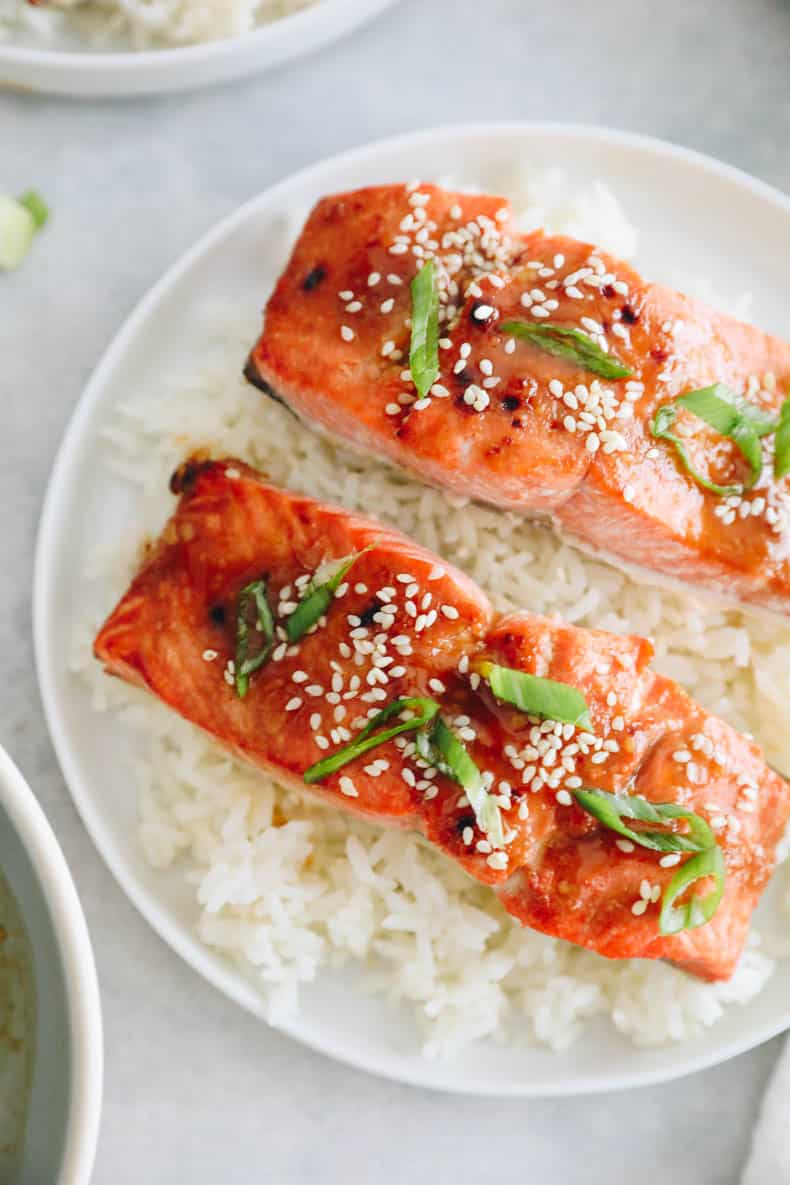 Salmon recipe with miso glaze on a bed of rice on a white plate.  Salmon is sprinkled with sesame and green onions.