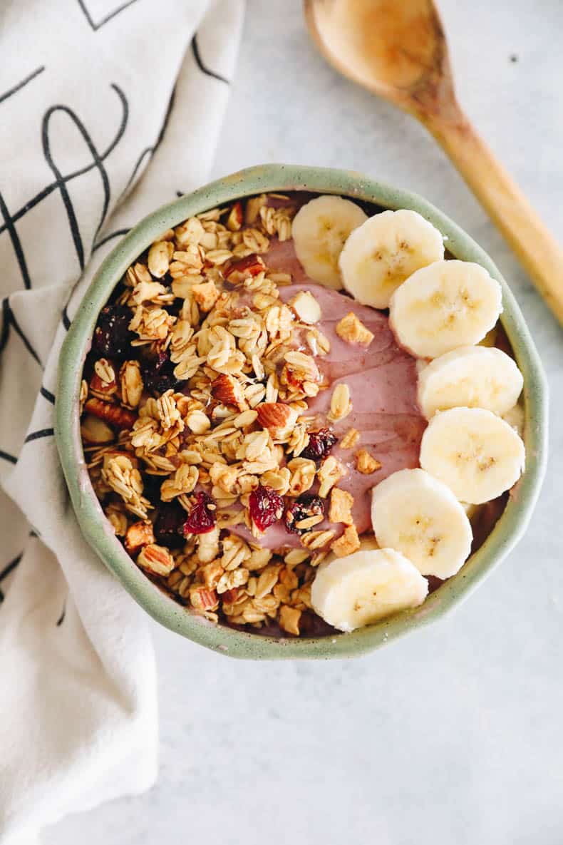pink smoothie bowl with banana and granola topping.