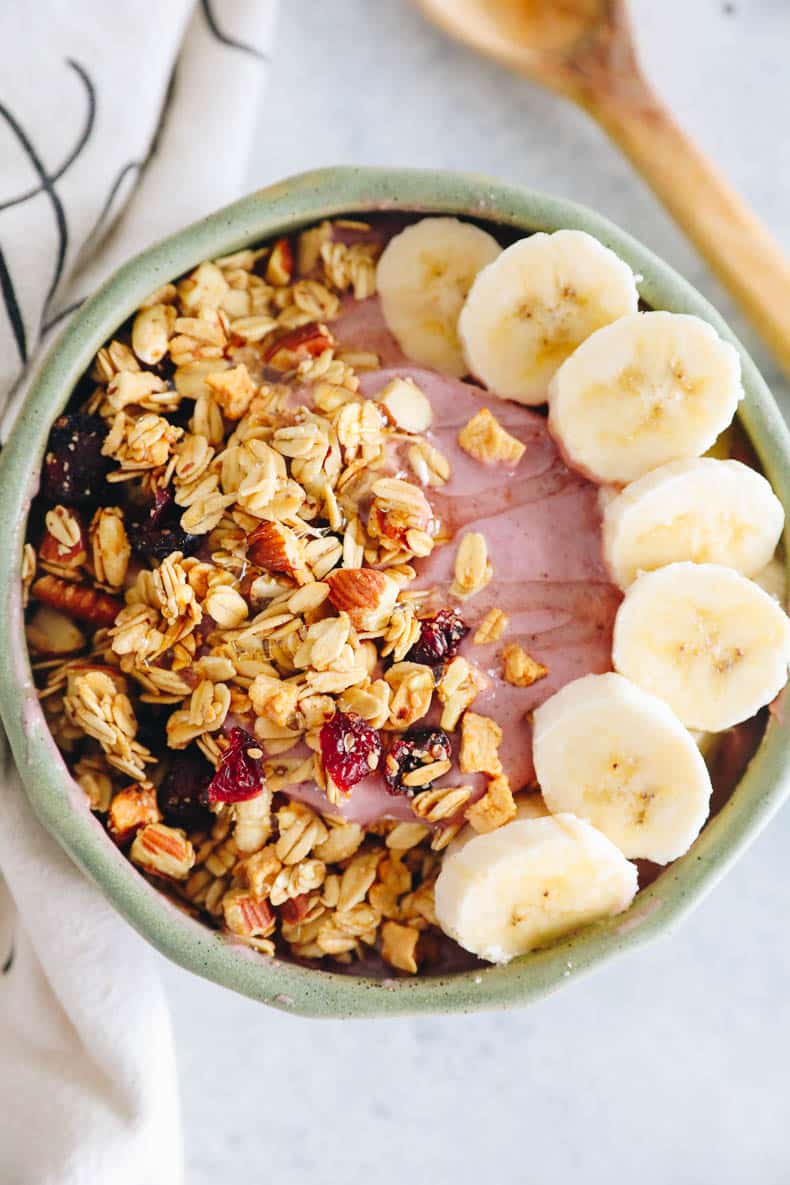 overhead image of pink raspberry smoothie bowl recipe topped with granola and banana.