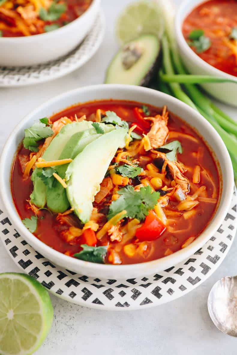 enchilada soup in a white bowl topped with avocado, shredded cheese and cilantro.