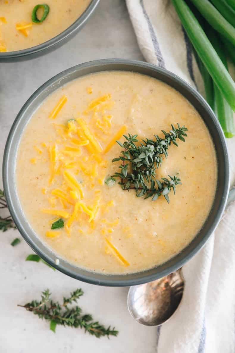 roasted cauliflower soup in a blue bowl topped with fresh thyme and cheddar cheese.