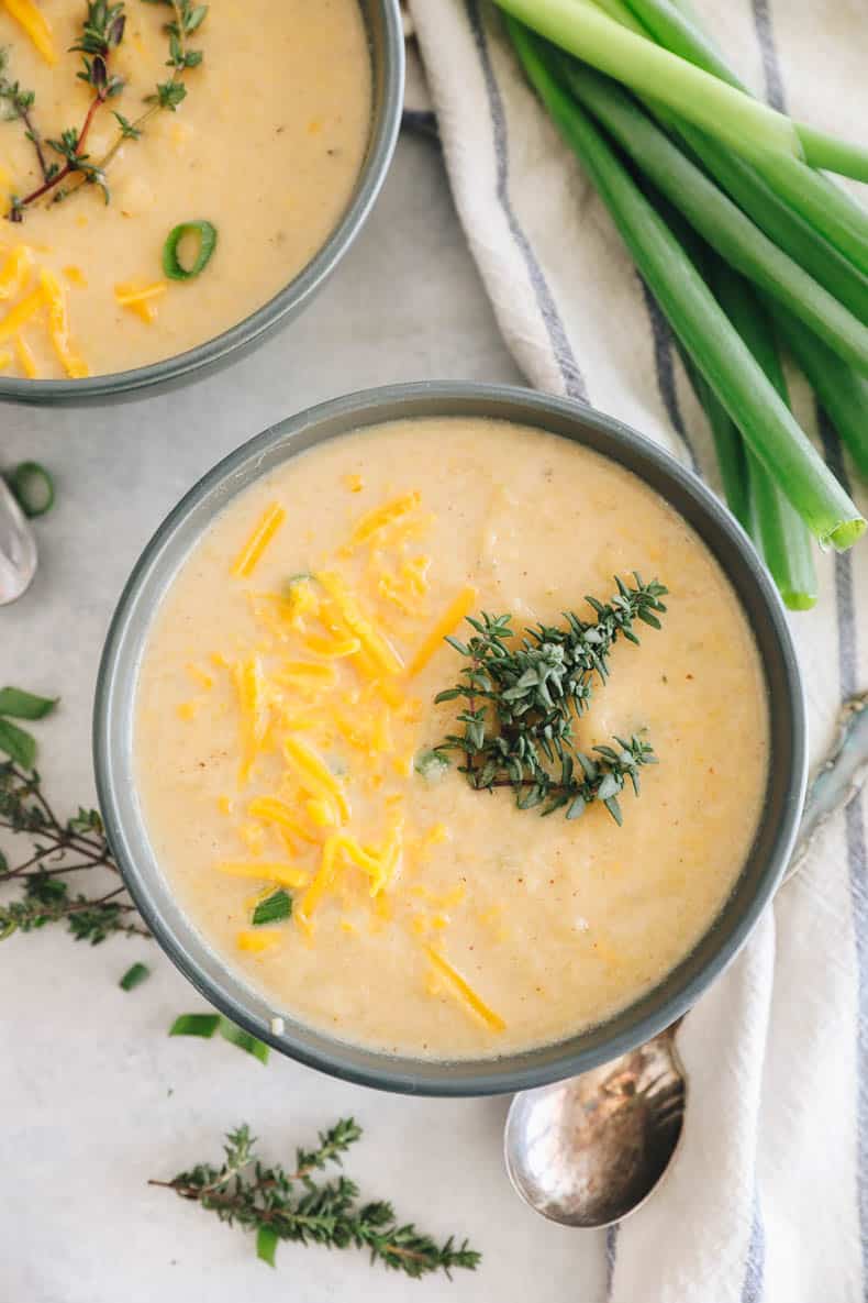 roasted cauliflower soup in a blue bowl topped with fresh thyme and cheddar cheese.