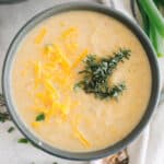 Roasted cauliflower soup in a blue bowl with fresh thyme and cheddar cheese.