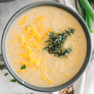 roasted cauliflower soup in a blue bowl topped with fresh thyme and cheddar cheese.