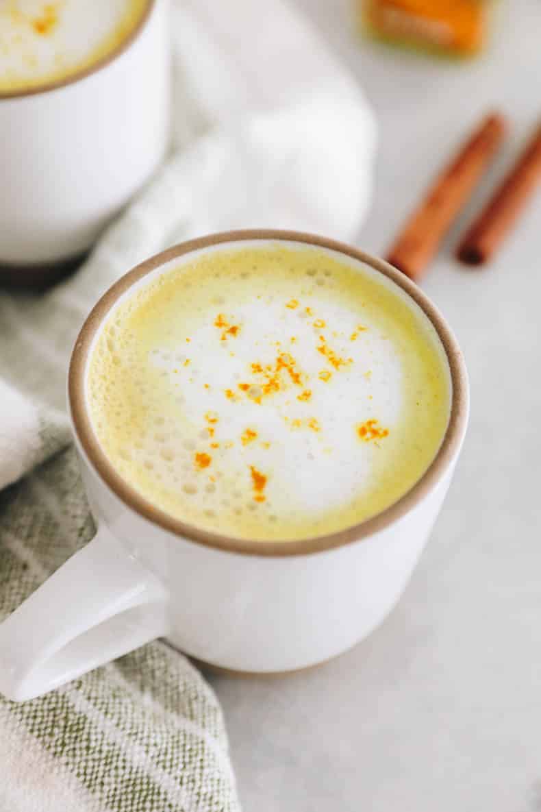 Turmeric latte in a white mug with foam and a pinch of turmeric powder.