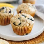 3 banana blueberry muffins in paper muffin liners on a white plate
