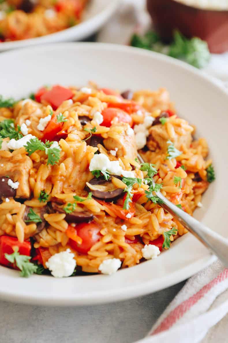 Greek chicken orzo plated in a white shallow bowl topped with parsley and feta.