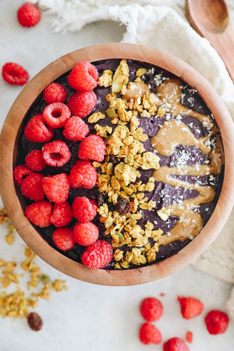 overhead shot of an acai bowl topped with raspberries, granola and nut butter.