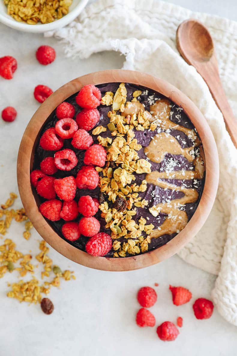 acai bowl recipe in a wooden bowl topped with raspberries, granola and almond butter.