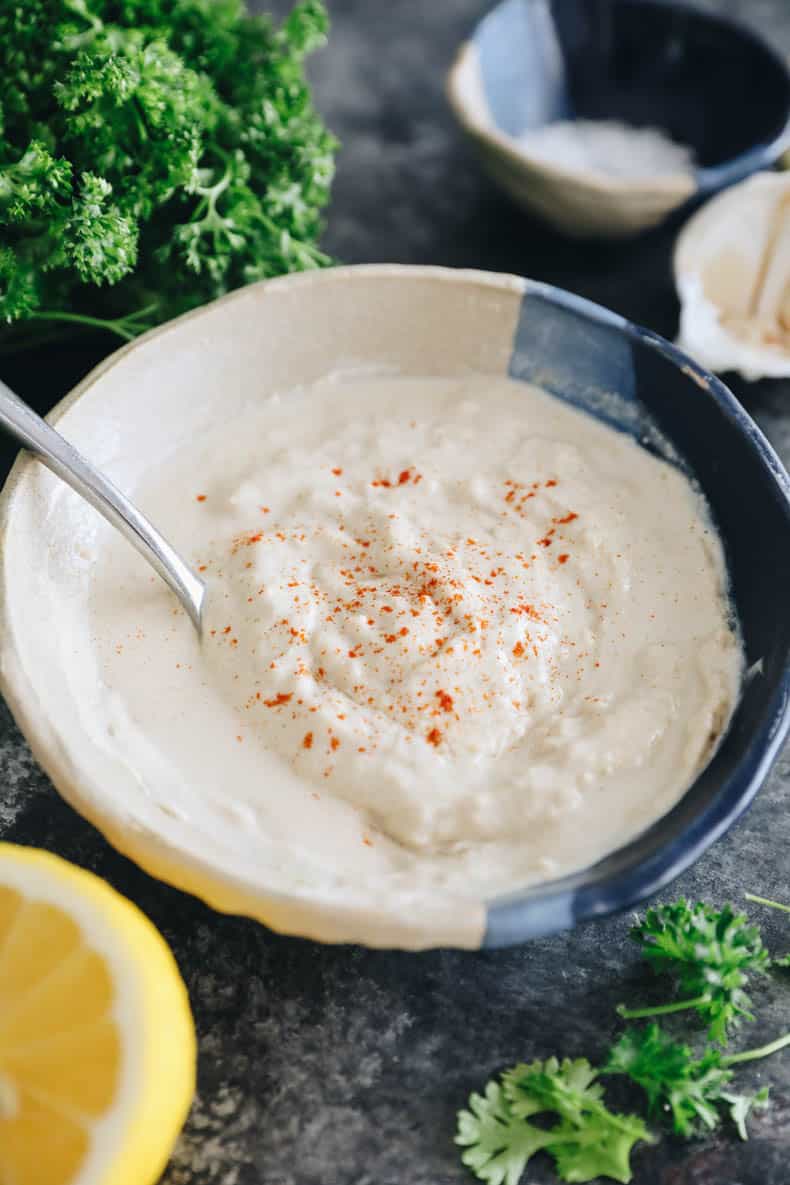 tahini sauce in a blue and white bowl with lemon and parsley scattered.