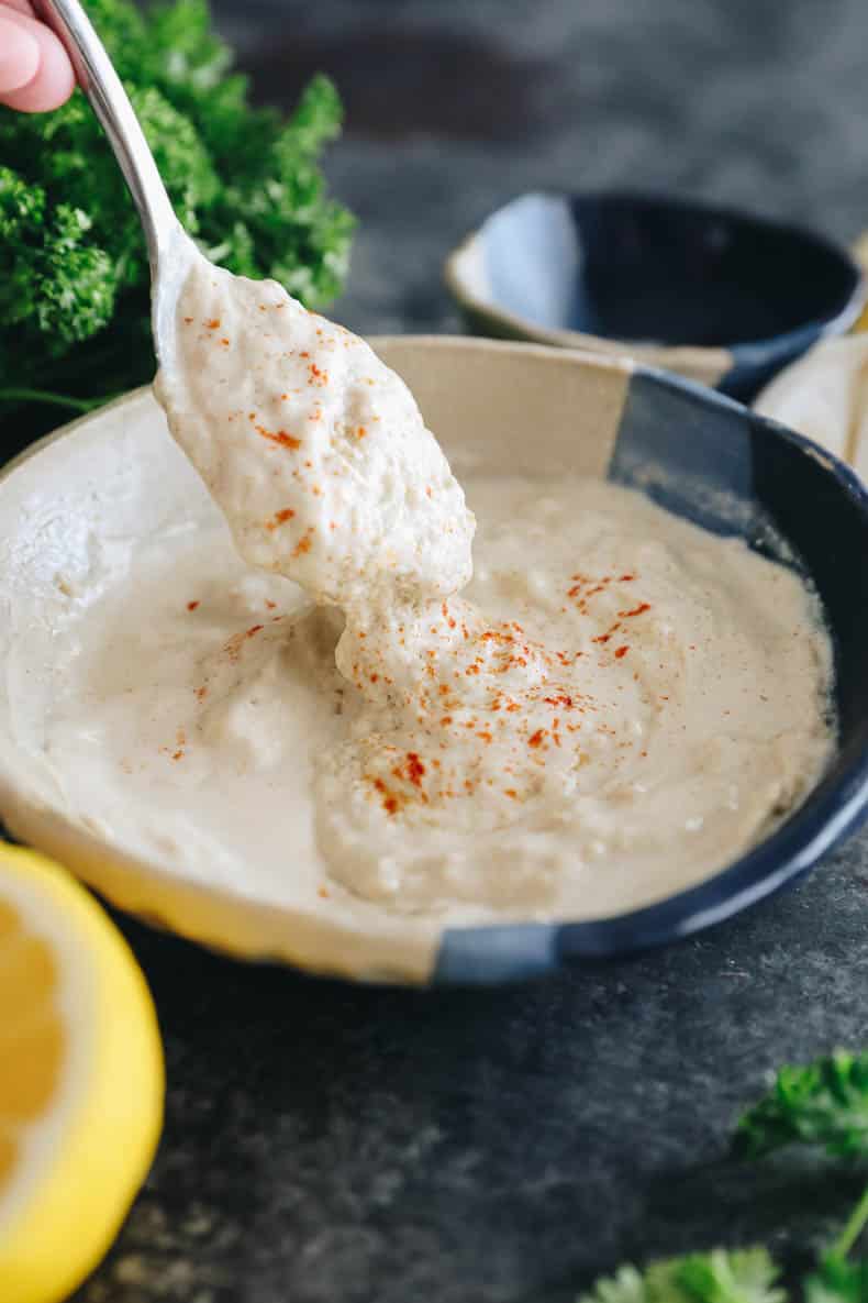 A spoon being picked up from a bowl with tahini sauce.