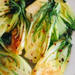 pan fried garlic baby bok choy on a plate with red pepper flakes.