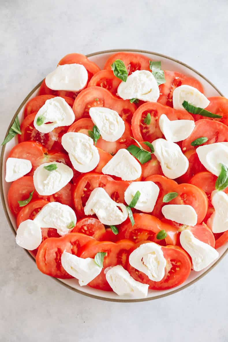 Tomatoes and burrata on a large platter sprinkled with basil leaves.