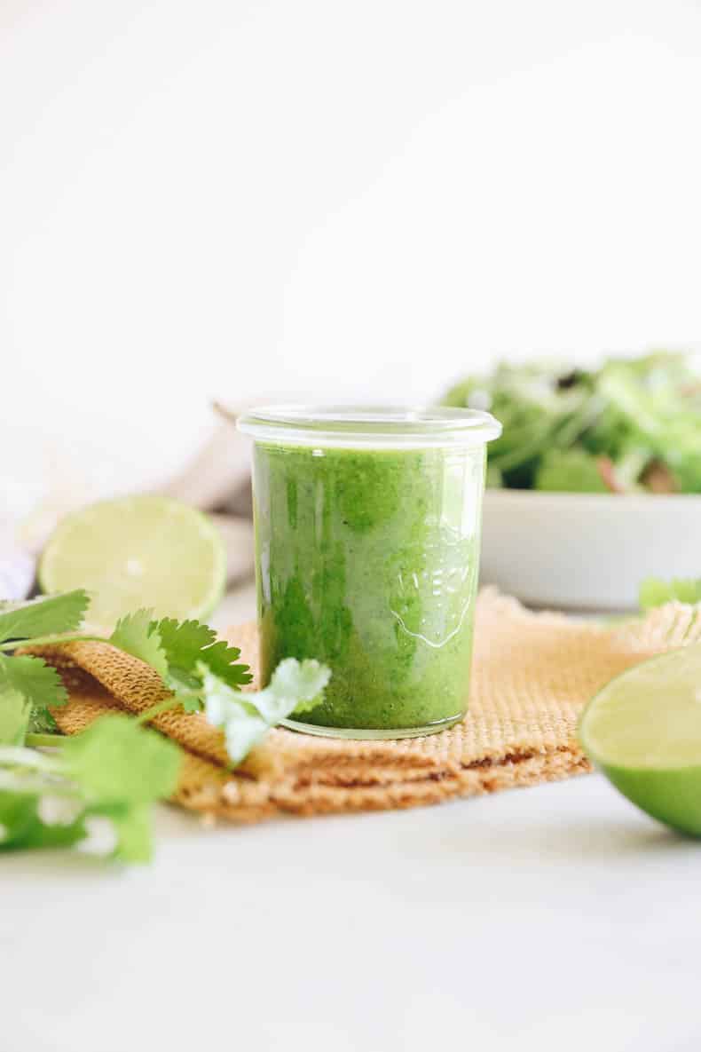 cilantro lime dressing in a small mason jar in front of a salad.