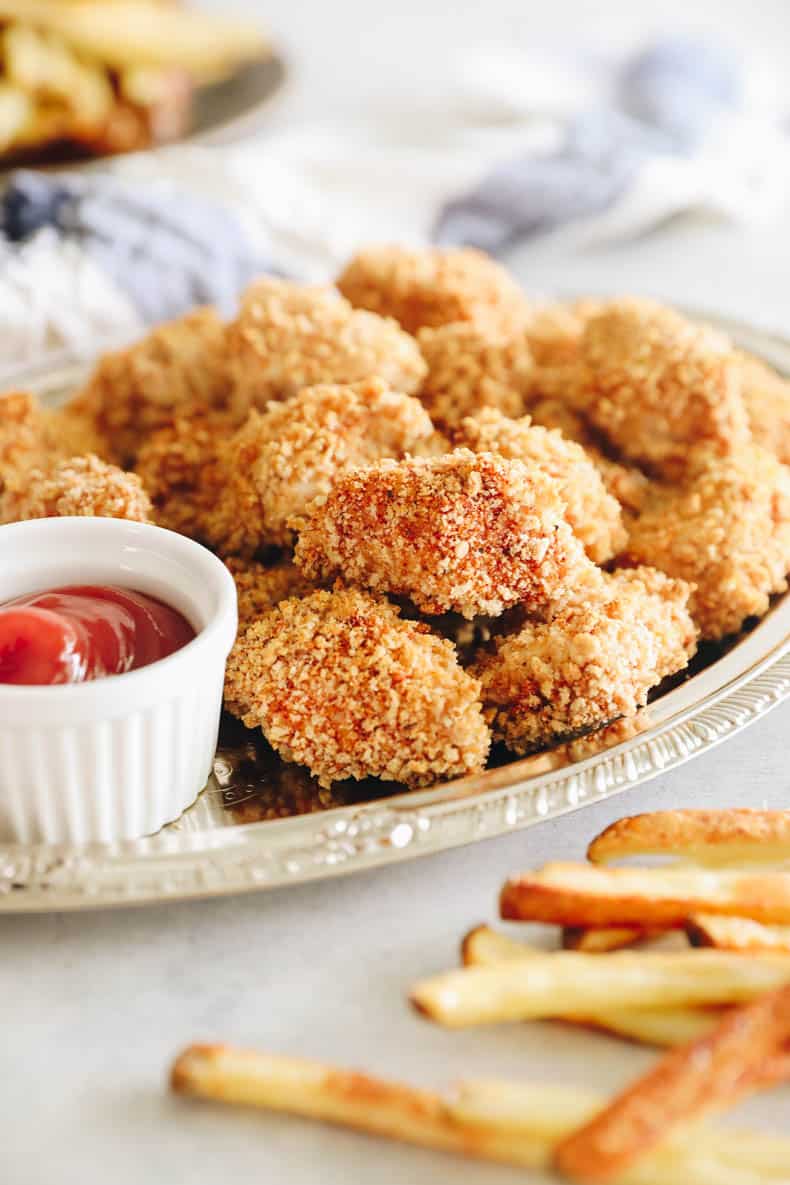 Homemade chicken nuggets on a silver platter with ketchup and french fries.