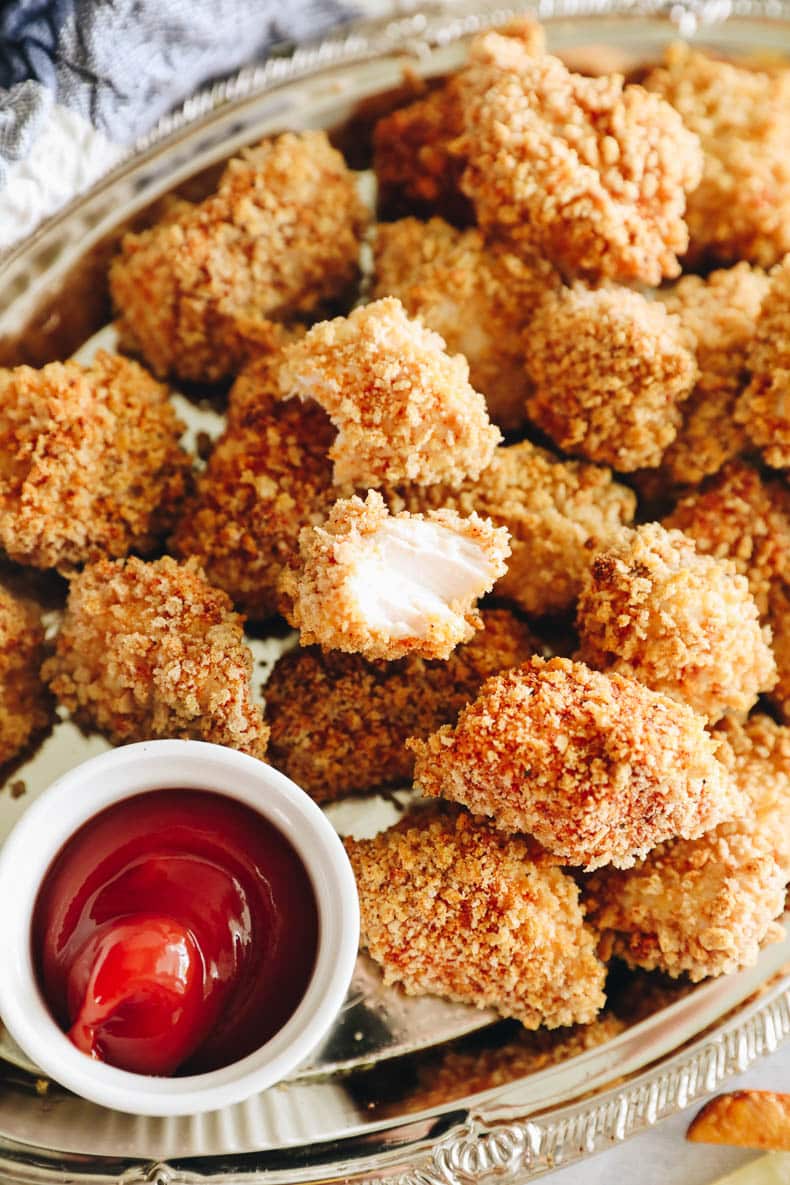 chicken nugget recipe with a bite in it on a silver platter with ketchup.