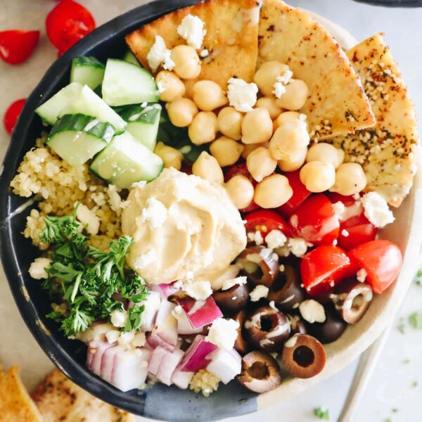 overhead photo of a mediterranean quinoa bowl with pita chips, hummus, tomatoes, cucumbers, red onion and olives.