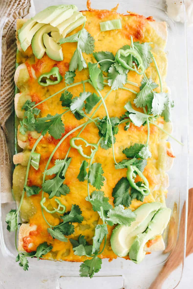 Green chicken tortillas in a glass pyrex dish with cilantro, cheese and avocado.