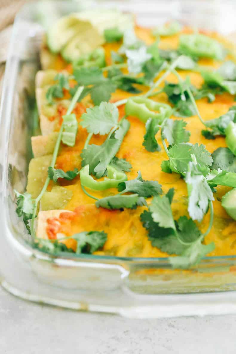 green chicken enchiladas topped with cheese and baked in a pyrex dish.
