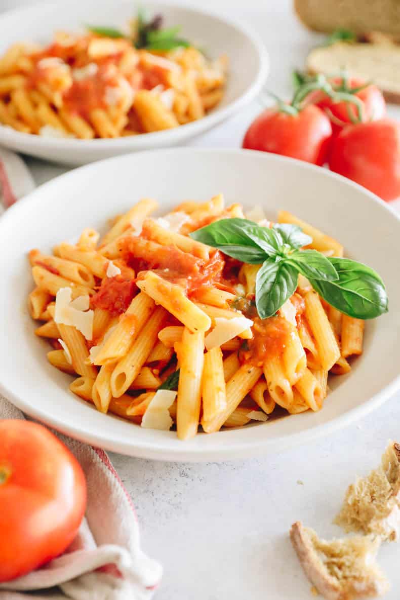Home made tomato sauce on penne pasta in a white shallow bowl with basil.