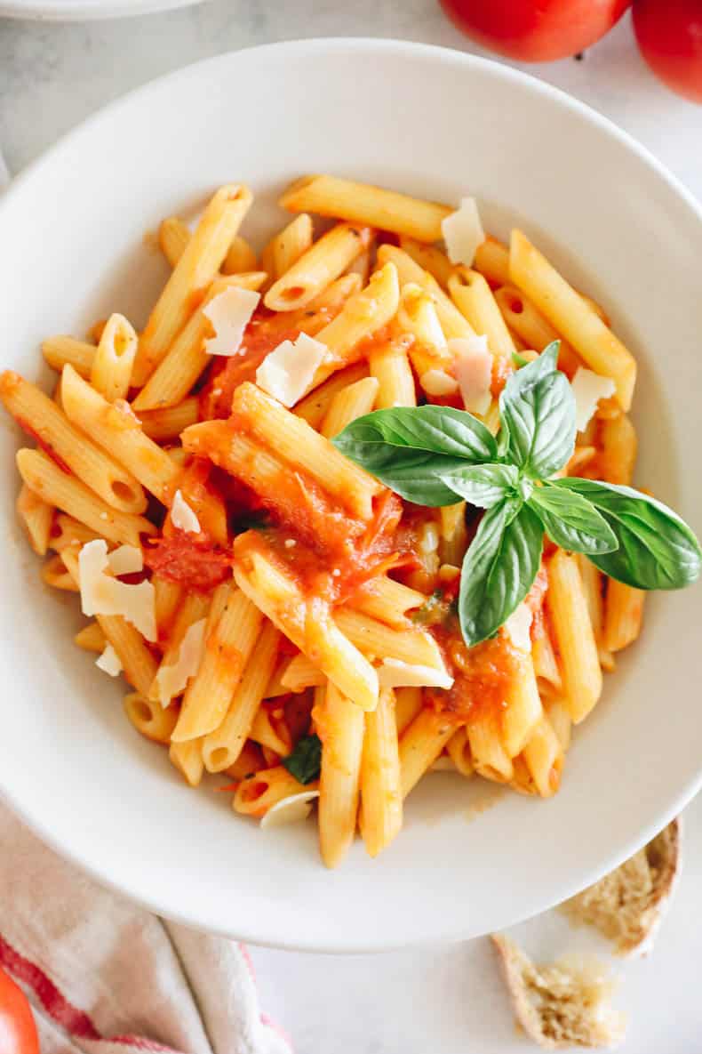 Big bowl of penne pasta topped with homemade tomato sauce, parmesan and basil.