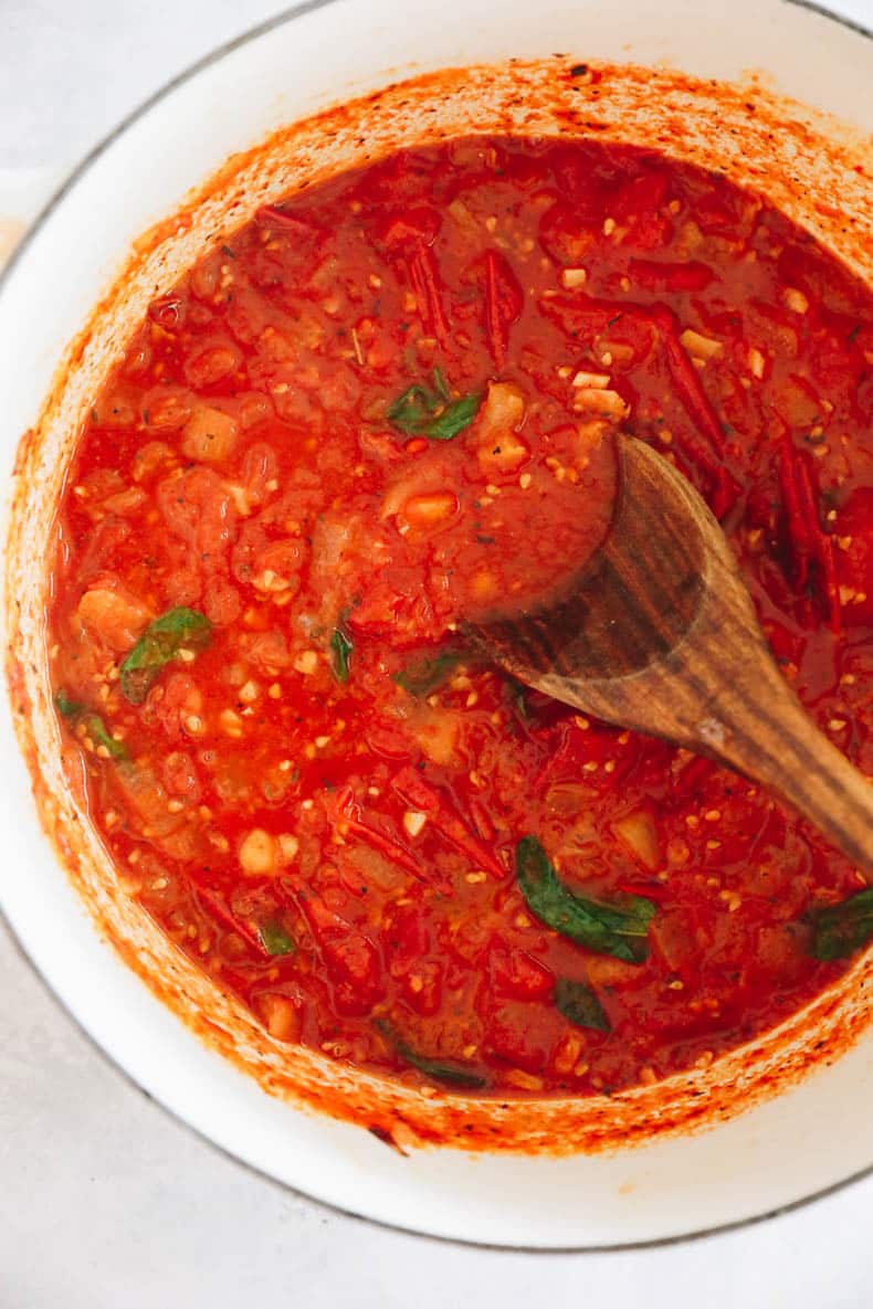 homemade tomato sauce in a large dutch oven with basil leaves.