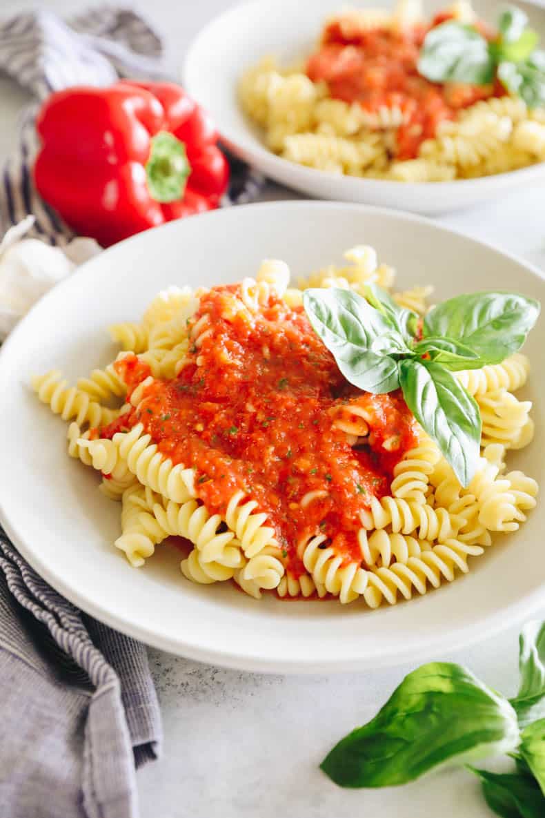 roasted red pepper sauce over fusilli in white shallow bowl with basil.