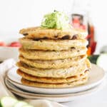 zucchini pancakes on a plate with shredded zucchini on top.