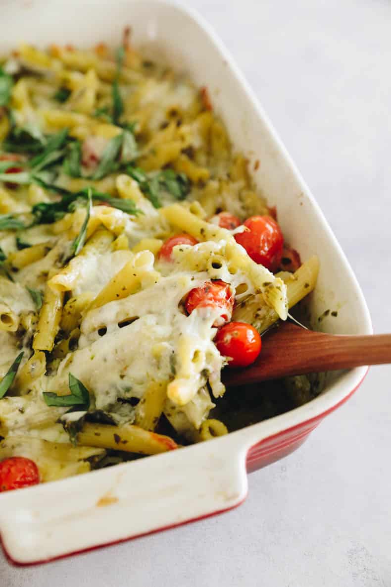 scooping out penne pasta from a baked pesto pasta dish.