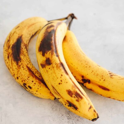 3 ripe bananas with brown spots on a white board.